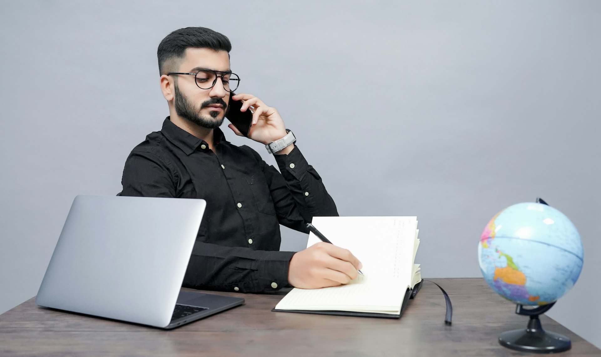 Un hombre sosteniendo un bolígrafo, un libro y una computadora portátil.